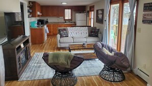 A cozy living room with a sofa, two armchairs, a coffee table, and a TV. There's a kitchen area with wooden cabinets and a refrigerator. - Cozy Cabin lake front (Dalbo)