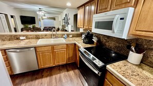 Une cuisine moderne avec des meubles en bois, un lave-vaisselle en acier inoxydable, une cuisinière noire et un four à micro-ondes blanc.