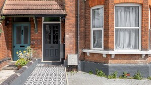 Ein zweistöckiges Backsteingebäude mit einer Fliesenveranda, einer grünen Tür und weiß gefassten Fenstern.
