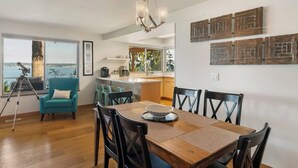Un comedor con una mesa y sillas de madera, un sillón color turquesa y un telescopio sobre un trípode.
