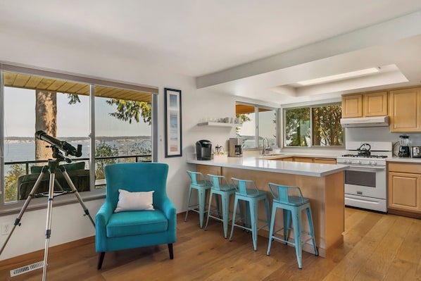 Una cocina moderna con una isla grande, taburetes de bar y un telescopio sobre un trípode.