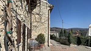 A stone building with a rustic appearance, a paved pathway, and a view of distant hills and a church tower.