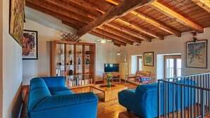 A spacious living room with wooden beams, blue sofas, a bookshelf, and a television.