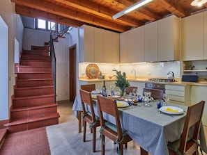 Un comedor con una escalera de madera, una cocina con estufa y alacenas, y una mesa de comedor lista para cuatro personas.