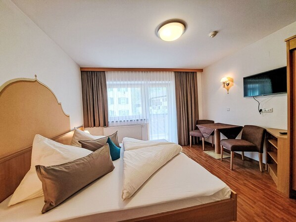 A hotel room with a bed, a desk, a chair, a television, and a window with curtains.