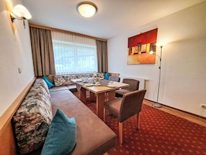 Quarto de hotel moderno com um sofá grande, uma mesa de jantar e um quadro na parede.