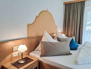 A hotel room with a wooden headboard, a bedside table with a lamp, and a bed with multiple pillows.