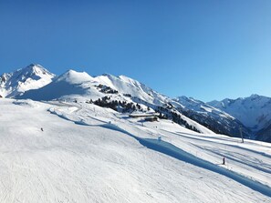 Paisagem montanhosa coberta de neve com pistas de esqui e céu azul límpido.
