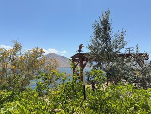 Una pérgola de madera con un pájaro posado, con vista a un lago y montañas al fondo.
