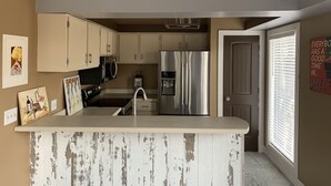 Een keuken met een centraal eiland, roestvrijstalen apparatuur en een groot raam met zonwering.
