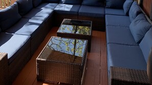 Een overdekt terras met een ruime modulaire bank en een salontafel met glazen blad.
