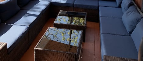A covered outdoor seating area with a large sectional sofa and a glass-top coffee table.