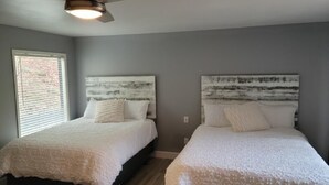 Een slaapkamer met twee bedden, een plafondventilator en een raam met jaloezieën.