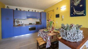A kitchen with blue cabinets, a dining table with a floral centerpiece, and a wall-mounted artwork. - Rebecca's House among the greenery, Bardonecchia, Italy (Bardonecchia)
