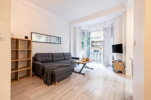 A modern living room with a grey sofa, wooden shelves, a small table with fruit, and a TV. - Appartement Shakespeare, Nice, France (Nice)