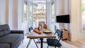 Un salon moderne comprenant un canapé, une table à manger, des chaises, un téléviseur à écran plat et une vue sur un balcon doté d’une balustrade.