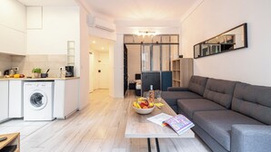 Un appartement moderne comprenant une cuisine, un espace de vie avec un canapé gris, une table à manger avec des fruits et un magazine, et un grand miroir au mur.