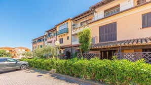 Una strada residenziale con un'auto parcheggiata, una fila di case con balconi e un siepe lungo il marciapiede.