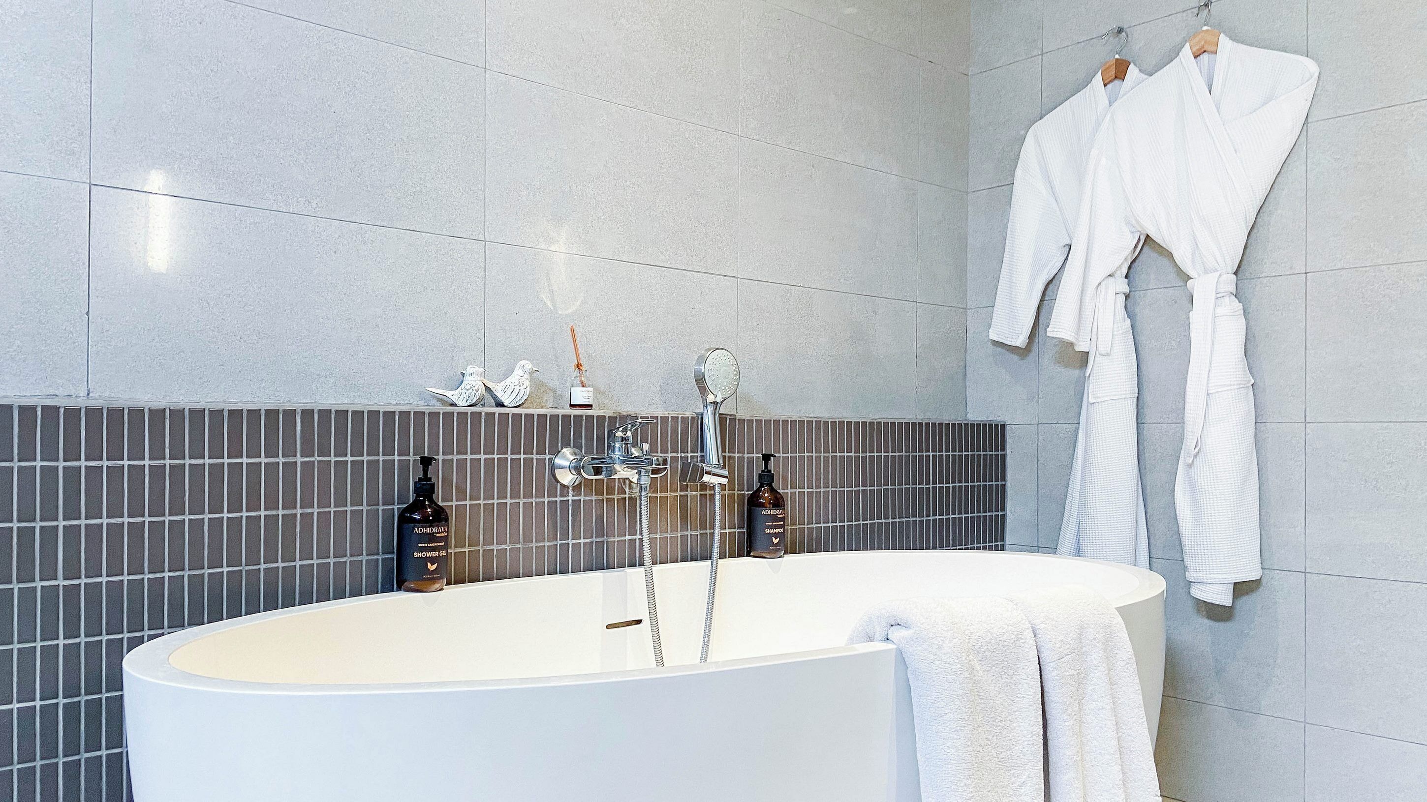 A modern bathroom with a freestanding bathtub, a showerhead, and two bottles of shampoo and shower gel.