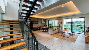 Un intérieur moderne avec un escalier, un espace de vie à aire ouverte, une cuisine et de grandes fenêtres donnant sur une piscine.