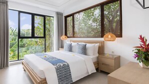 Une chambre moderne avec un grand lit, une tête de lit en bois et une vue sur une végétation luxuriante grâce à de grandes fenêtres.