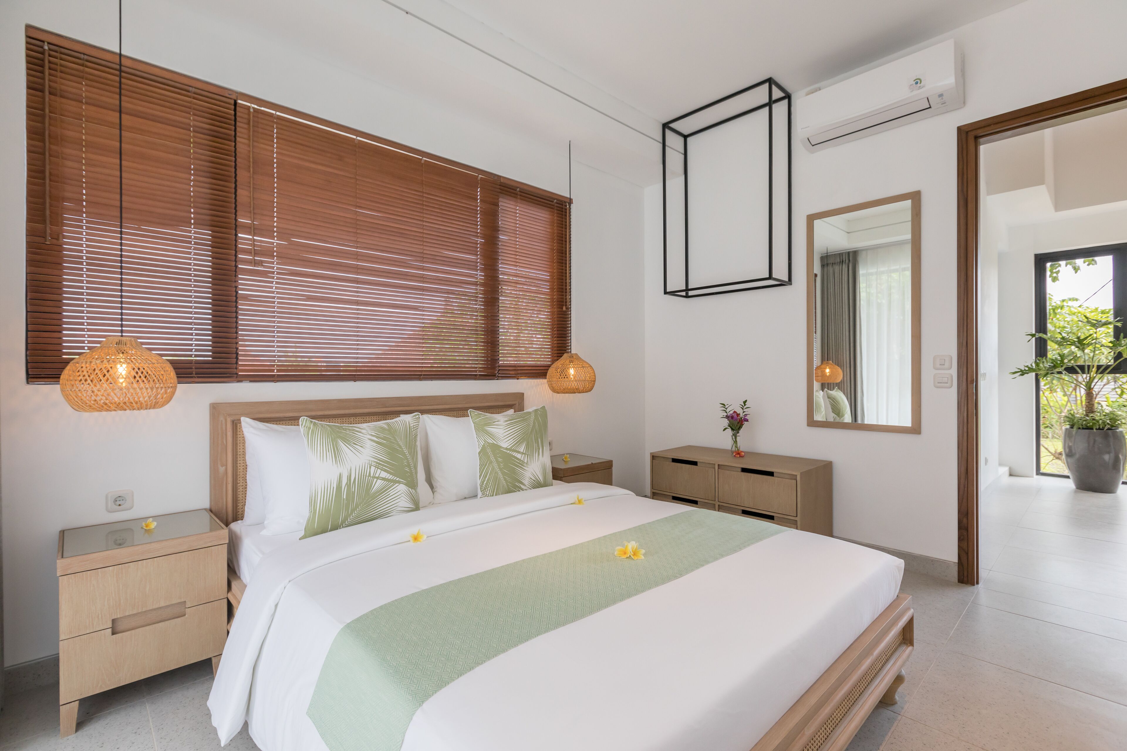 Un dormitorio moderno con una cama grande, cabecera de madera, dos mesitas de noche, un atril, un espejo y una planta en maceta.