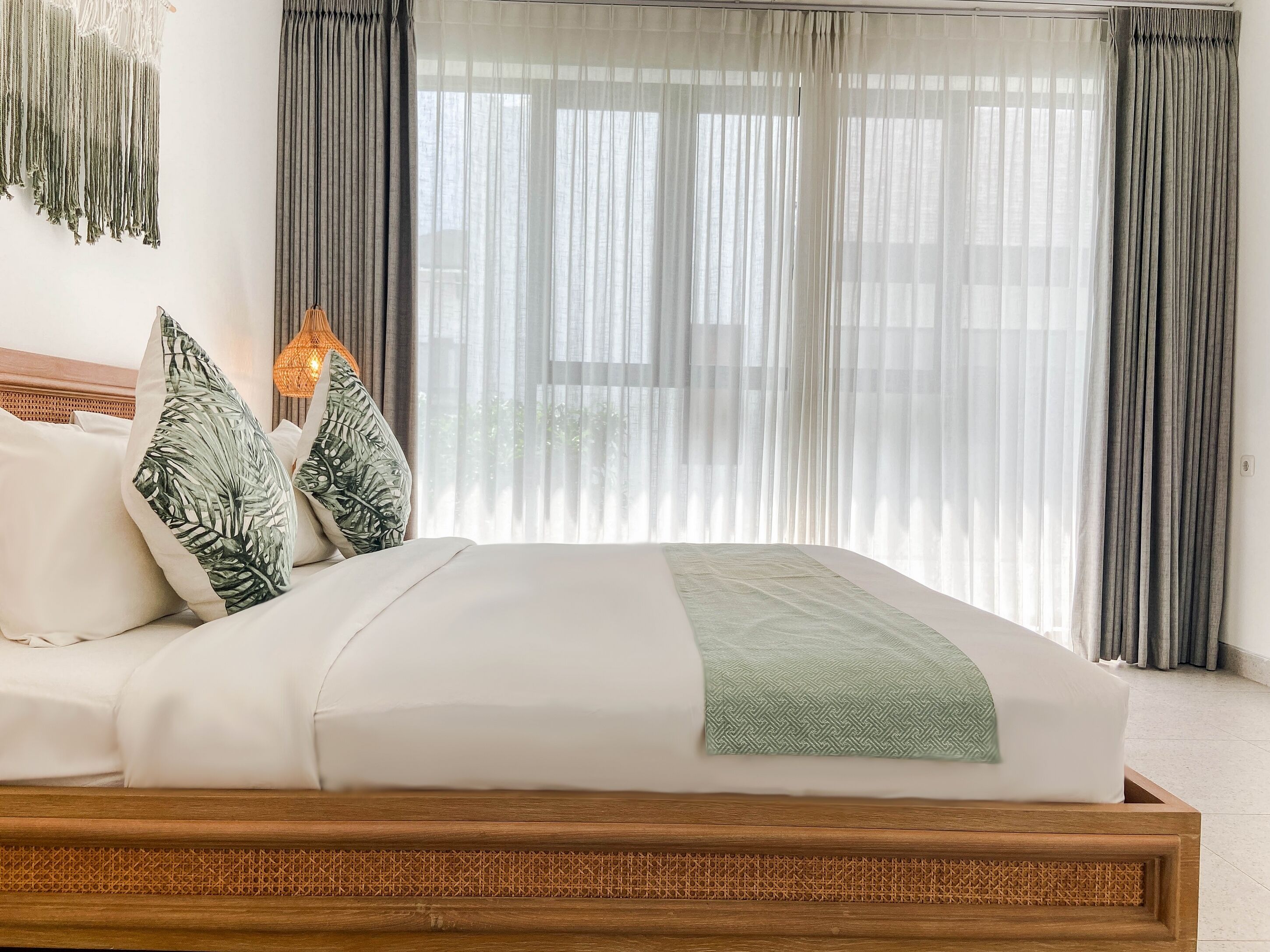 Una cama bien hecha con cabecera de madera, ropa de cama blanca y una manta verde.