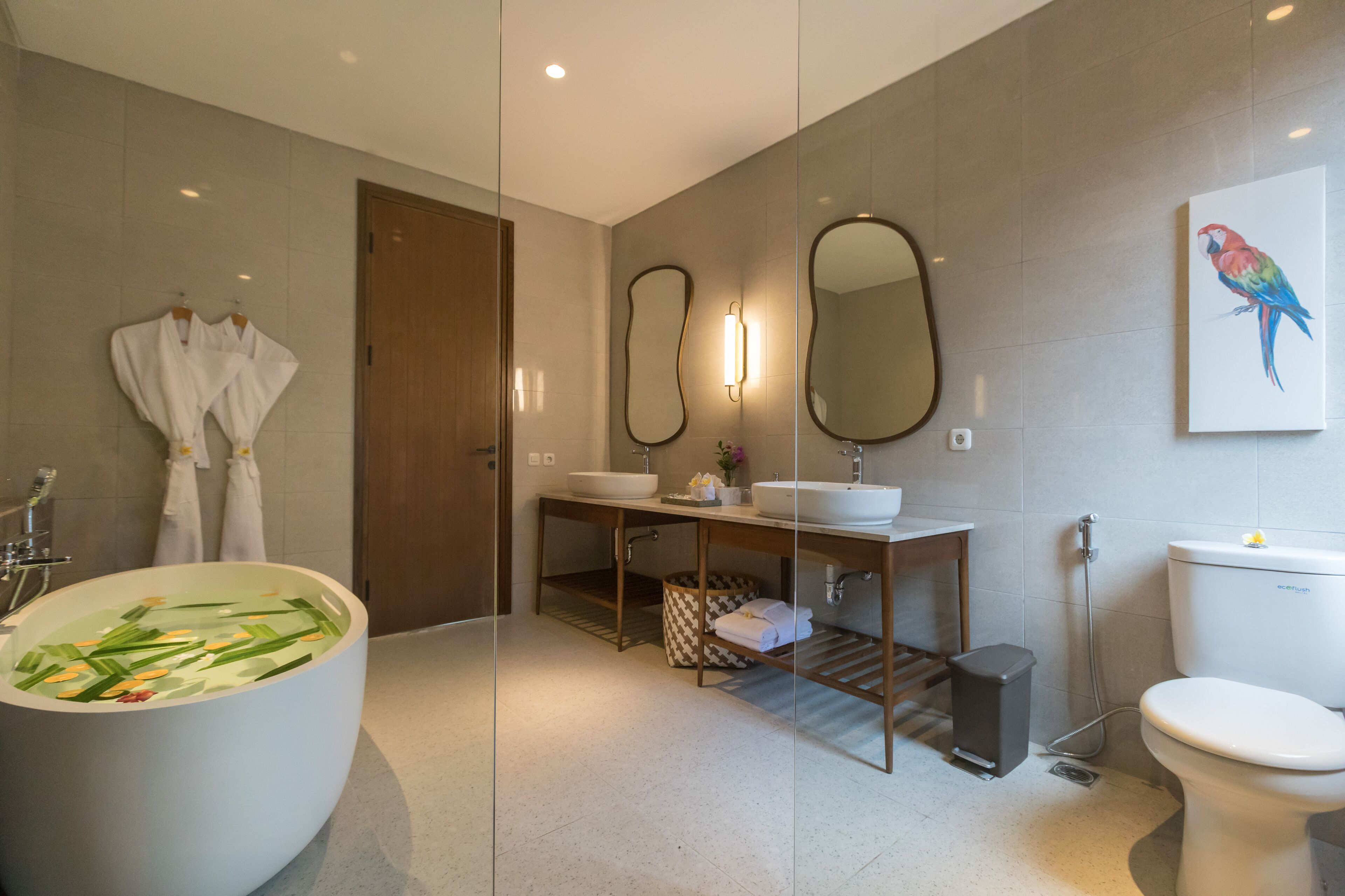 A modern bathroom with a freestanding bathtub, a wooden vanity with a mirror, a toilet, and a wall-mounted bird painting.