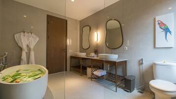 A modern bathroom with a freestanding bathtub, a wooden vanity with a mirror, a toilet, and a wall-mounted bird painting.