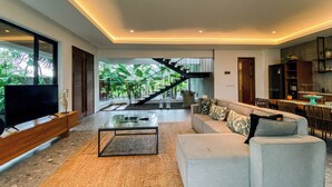 Un salon moderne doté d’un grand téléviseur, d’un canapé, d’une table basse et d’un escalier menant à un balcon agrémenté d’une végétation luxuriante.