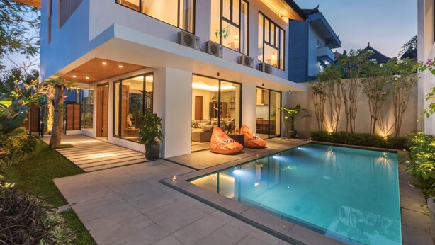 Une maison moderne à deux étages dotée d’une piscine, de grandes fenêtres et d’un espace salon extérieur.