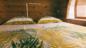 Une chambre rustique aménagée dans une cabane en bois, avec un lit recouvert d’une courtepointe à motifs de feuilles et deux oreillers bordés de jaune.