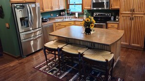 A kitchen with wooden cabinets, stainless steel appliances, a central island with chairs, and a decorative vase with sunflowers. - Cozy Bear Paradise  on Weiss Lake  in the foothills of the Appalachian Mountains (Cedar Bluff)
