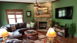 A living room with a stone fireplace, leather sofa, and a flat-screen TV mounted on the wall. - Cozy Bear Paradise  on Weiss Lake  in the foothills of the Appalachian Mountains (Cedar Bluff)