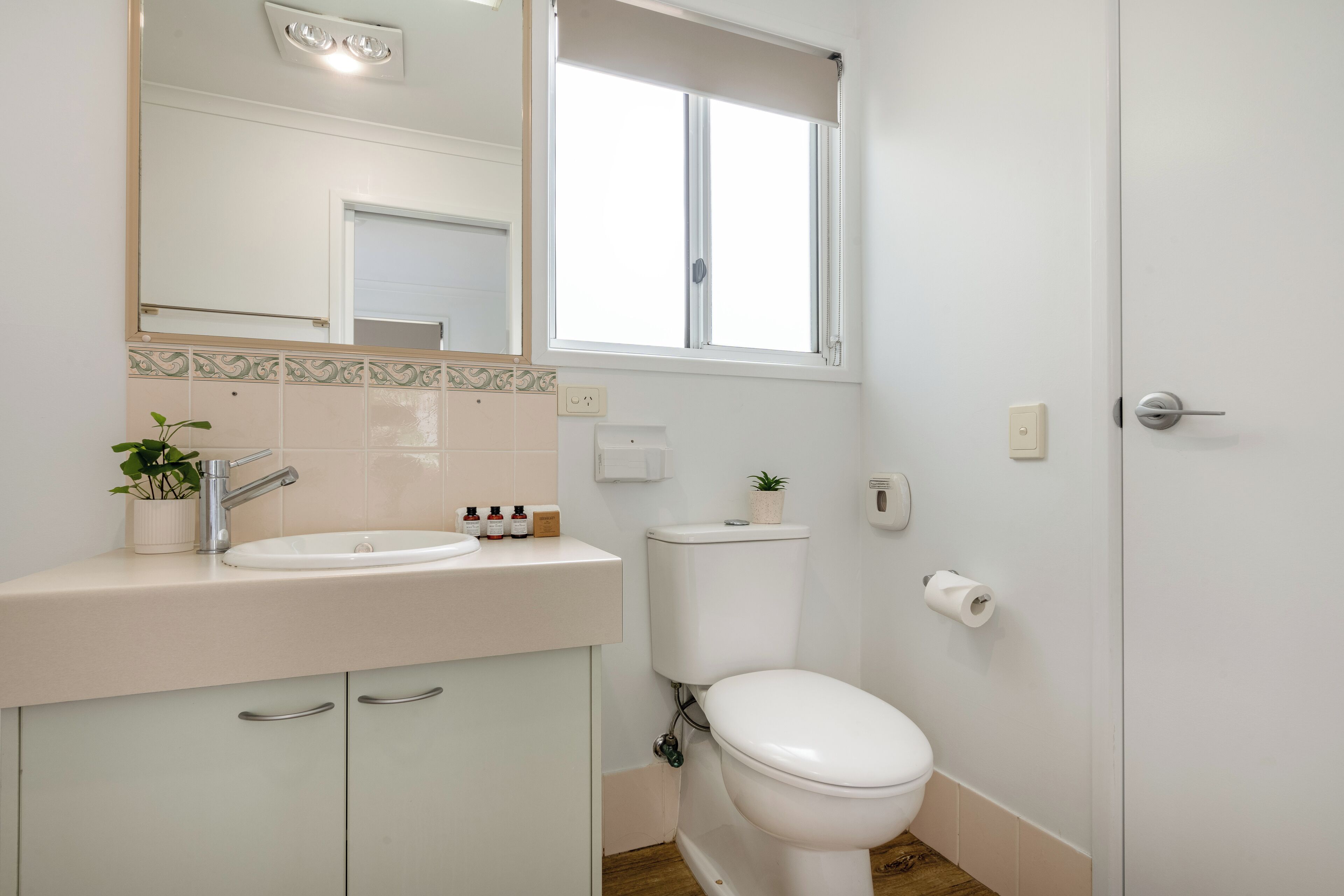 Een badkamer met een witte wastafel, toilet, spiegel en raam.