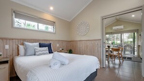 Un dormitorio con una cama grande, un cabecero de madera, una mesita de noche pequeña y una ventana.