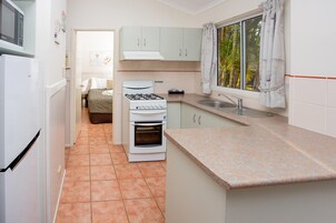 Cocina compacta con estufa, horno y lavamanos, comunicada con un pequeño comedor con mesa y sillas.
