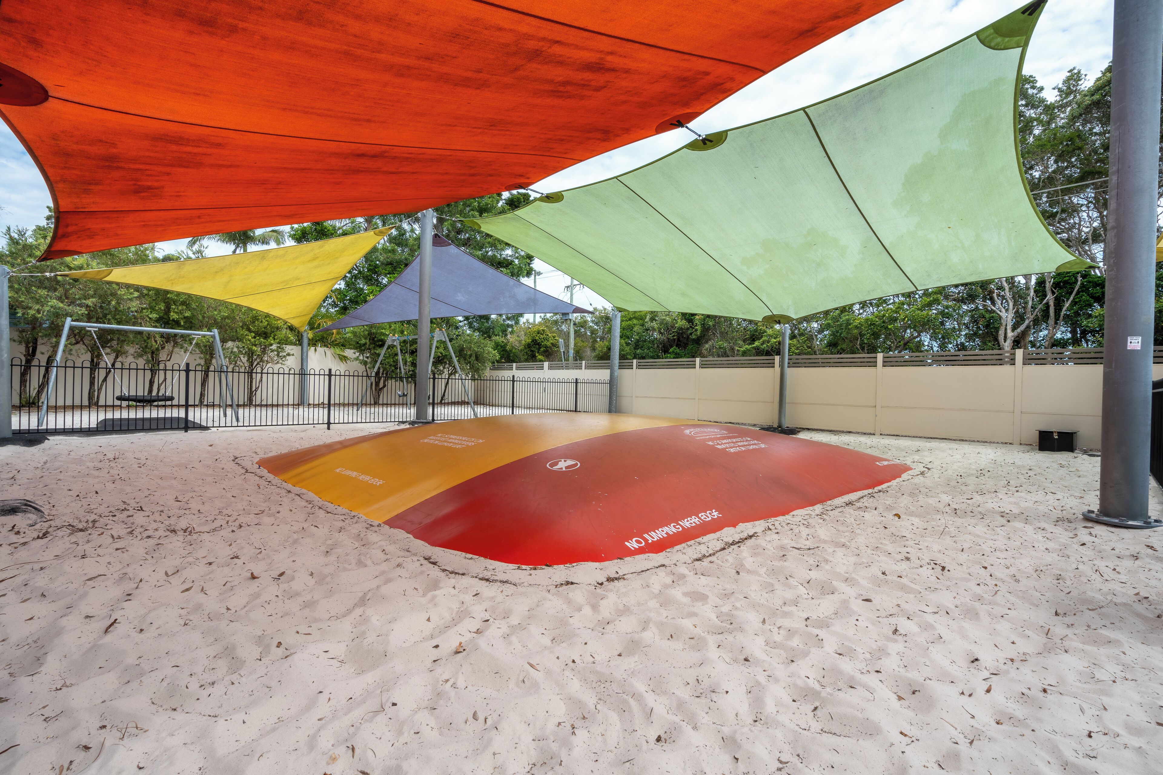 A sandy play area with multiple shaded sections and a red safety mat.