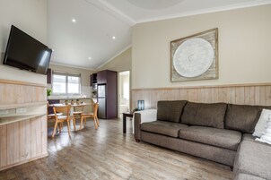 Una sala moderna con un sofá, una mesa de comedor con sillas, un televisor montado en la pared y un plato decorativo en la pared.