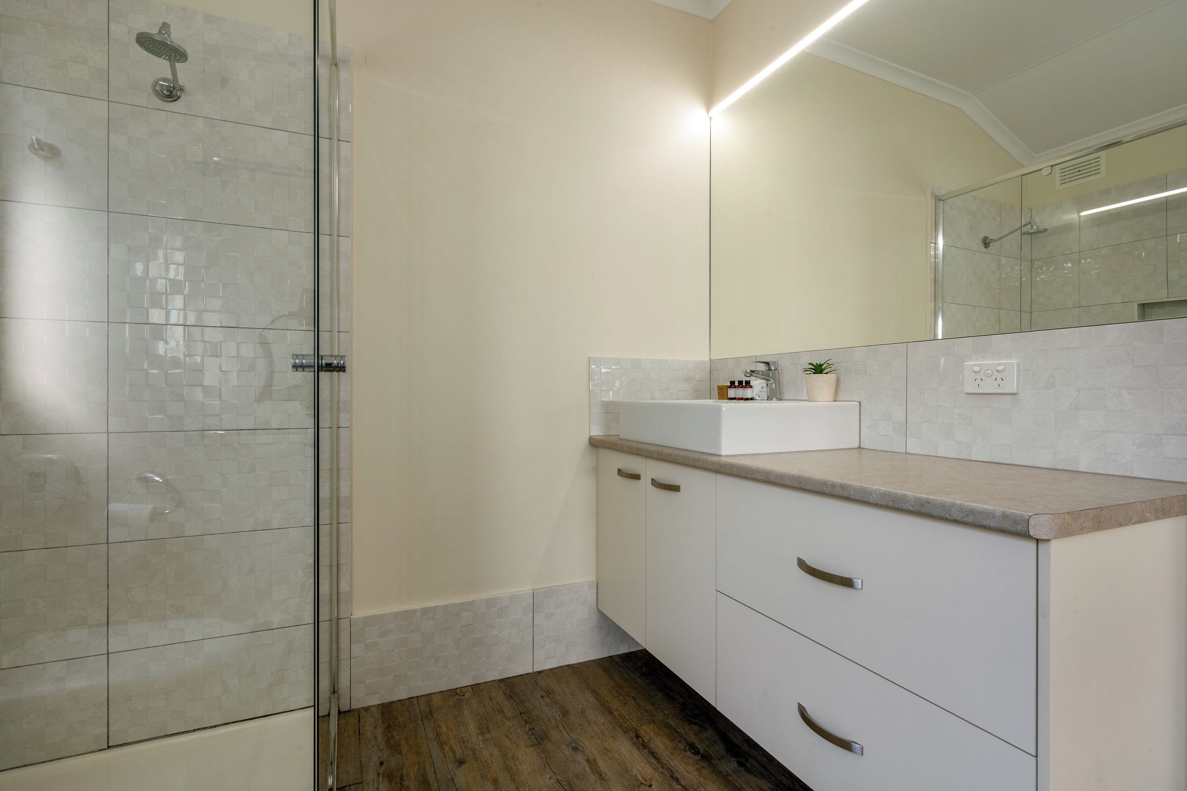 A modern bathroom with a glass shower enclosure, a white sink, and a large mirror.