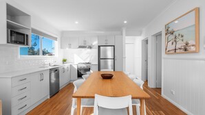 Una cocina moderna con armarios blancos, electrodomésticos de acero inoxidable y una mesa de comedor de madera con sillas blancas.