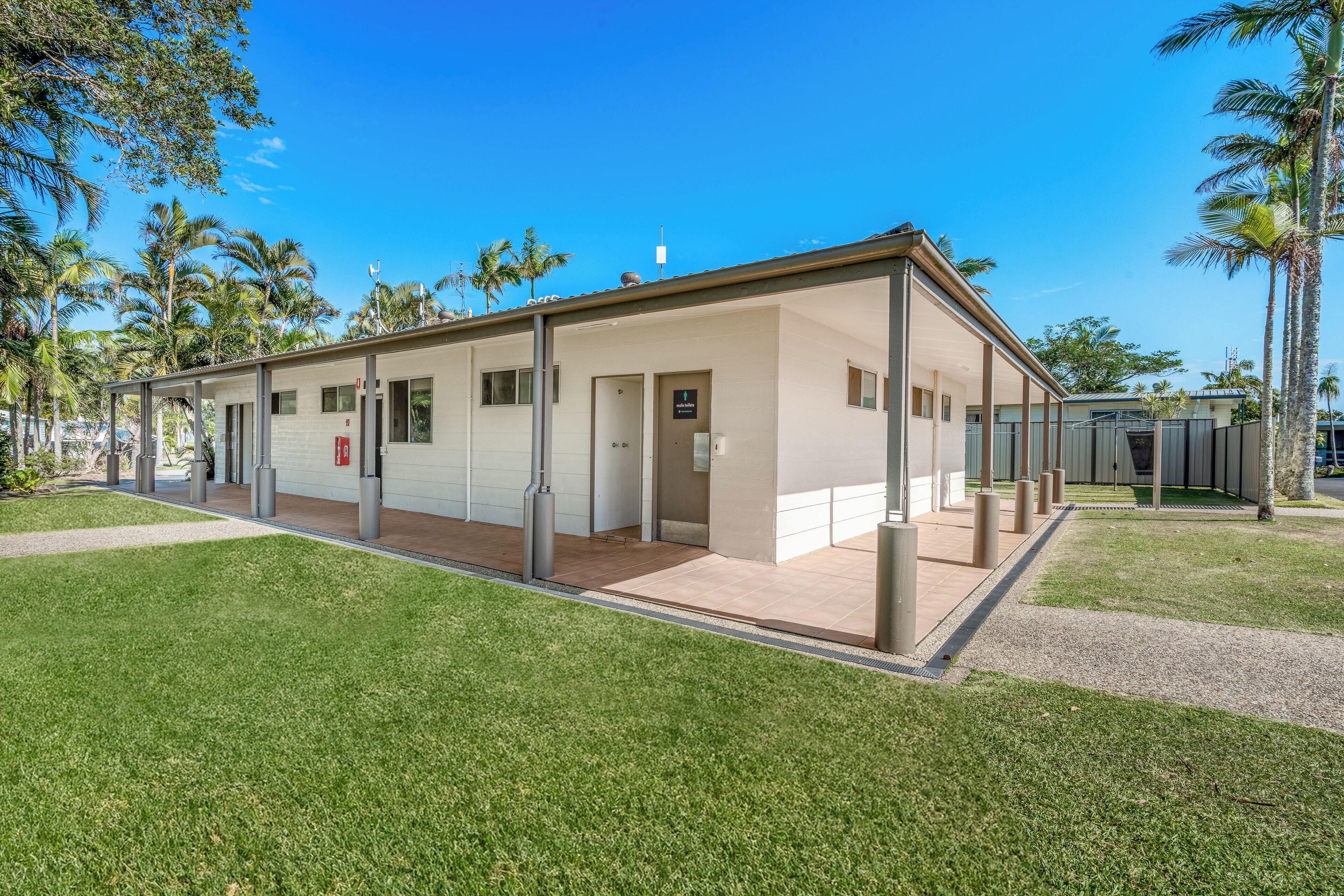 A modern building with a covered walkway, surrounded by palm trees and a well-maintained lawn.