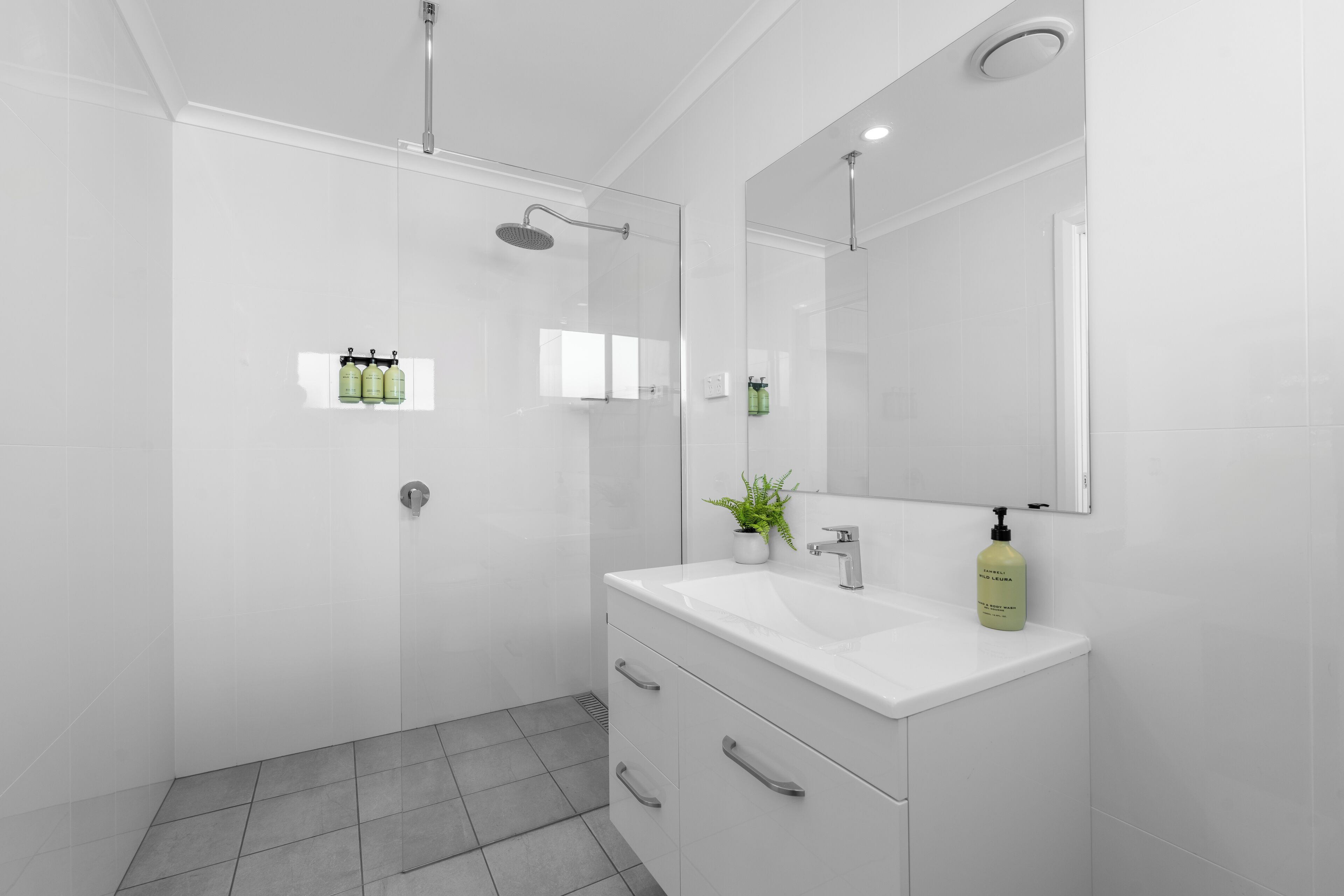 Un baño moderno con ducha envuelta en vidrio, un lavabo blanco con espejo y una planta en maceta.
