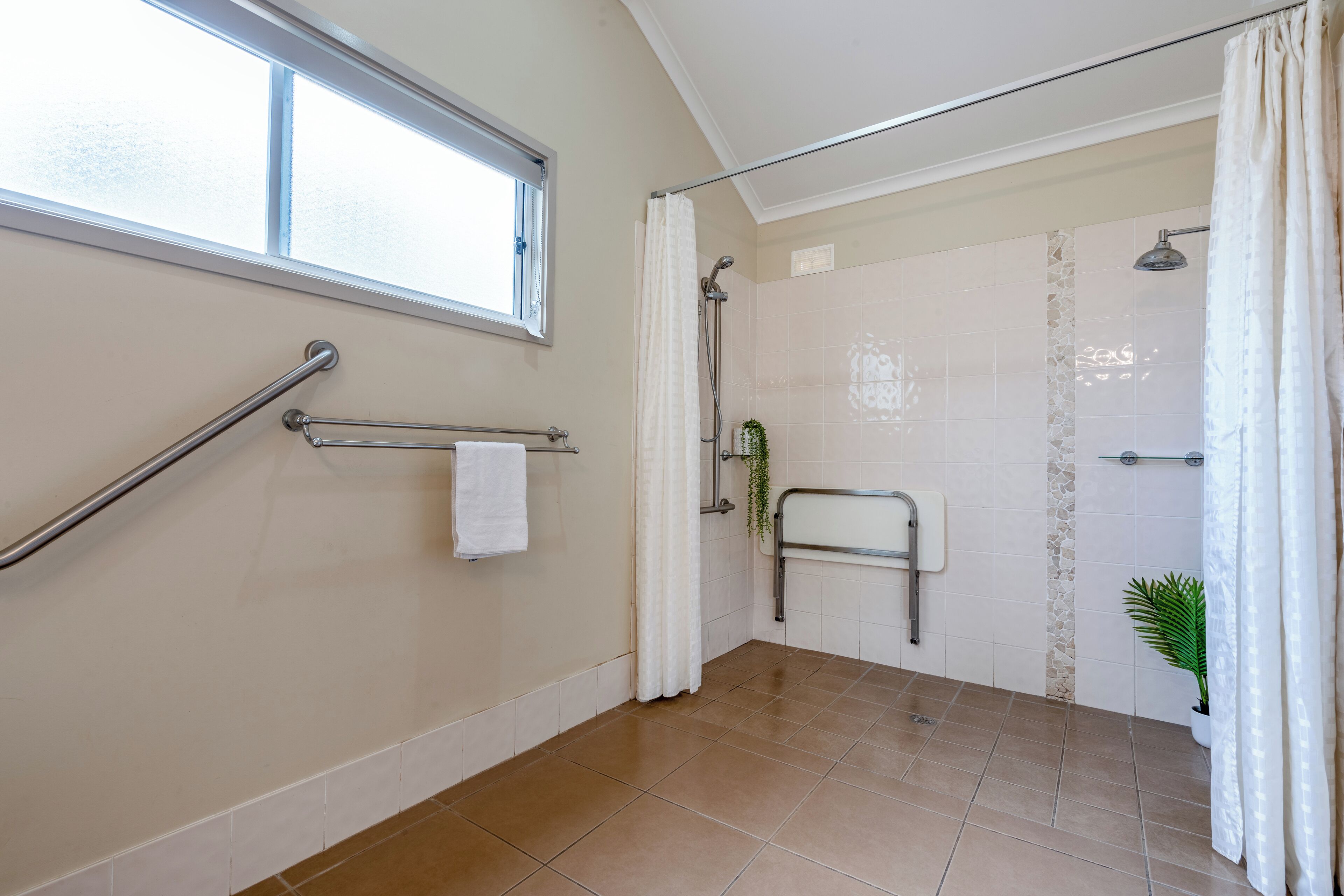 A modern bathroom with a shower, a handrail, a towel rack, and a window.