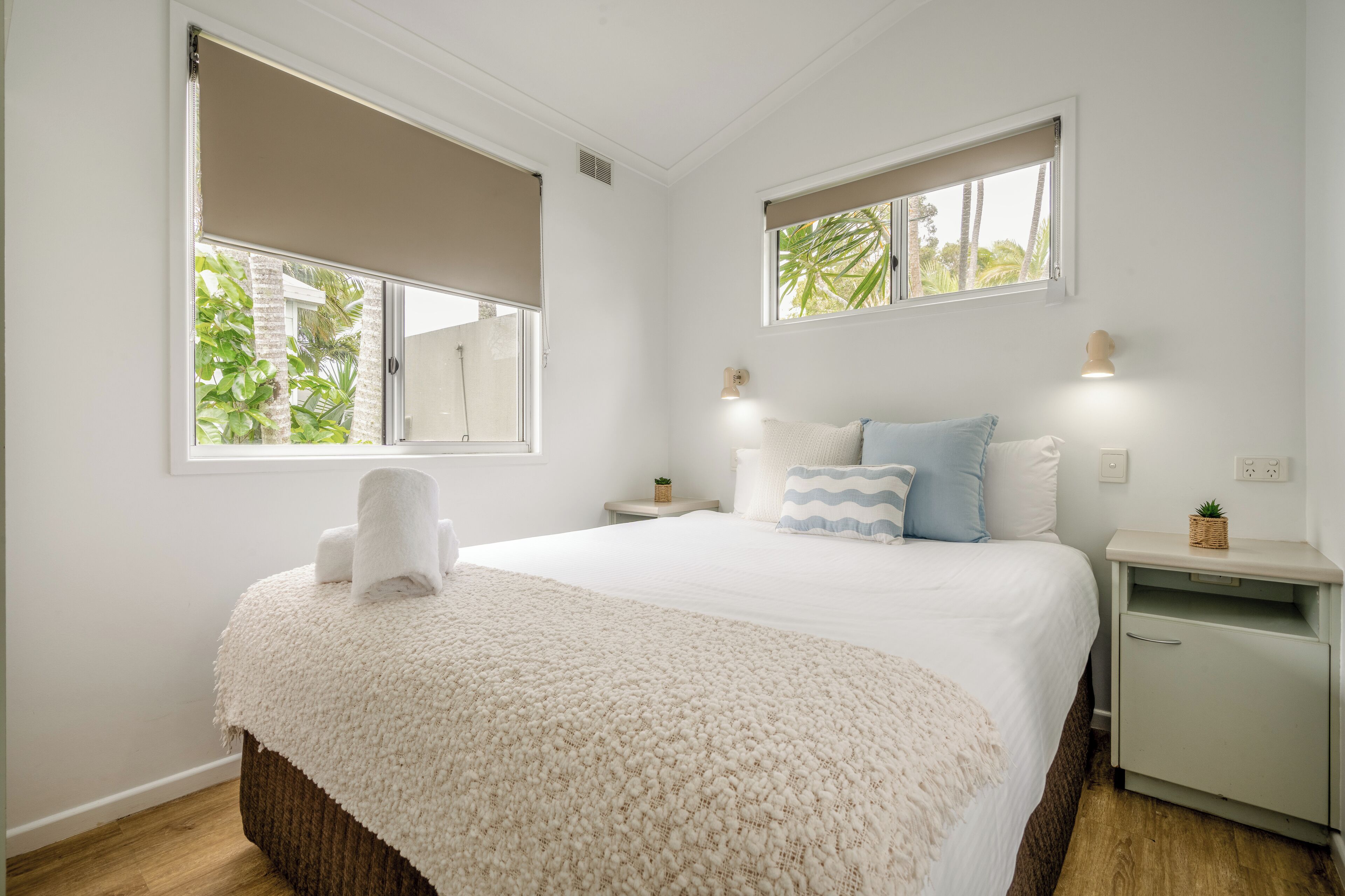 Une chambre à coucher avec un grand lit, deux tables de chevet, une commode et une fenêtre donnant sur un paysage verdoyant.