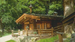 A rustic cabin with a wooden porch, surrounded by lush greenery. - Apartment Almbrünnerl 30 sqm, 1 bedroom, 1 living room/bedroom, kitchen, max. 2 p. (Ruhpolding)