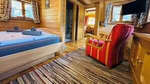 A wooden cabin room with a bed, a red upholstered chair, a television, and a wooden ceiling. - Apartment Almbrünnerl 30 sqm, 1 bedroom, 1 living room/bedroom, kitchen, max. 2 p. (Ruhpolding)