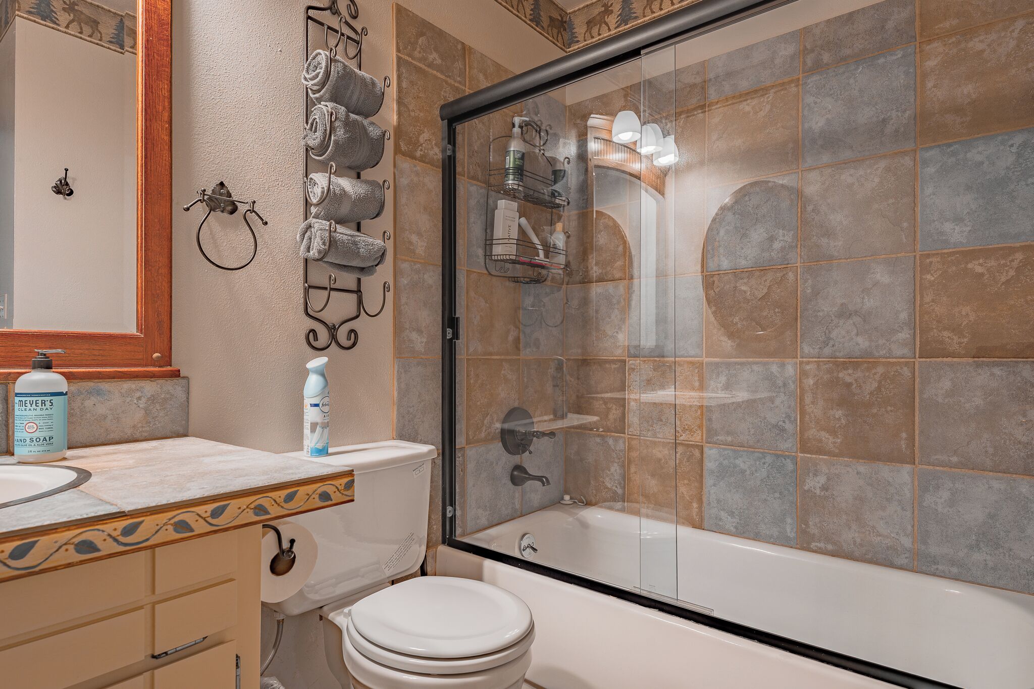 Une salle de bain dotée d’une douche à parois de verre, de toilettes et d’un lavabo avec un revêtement mural décoratif en carreaux.