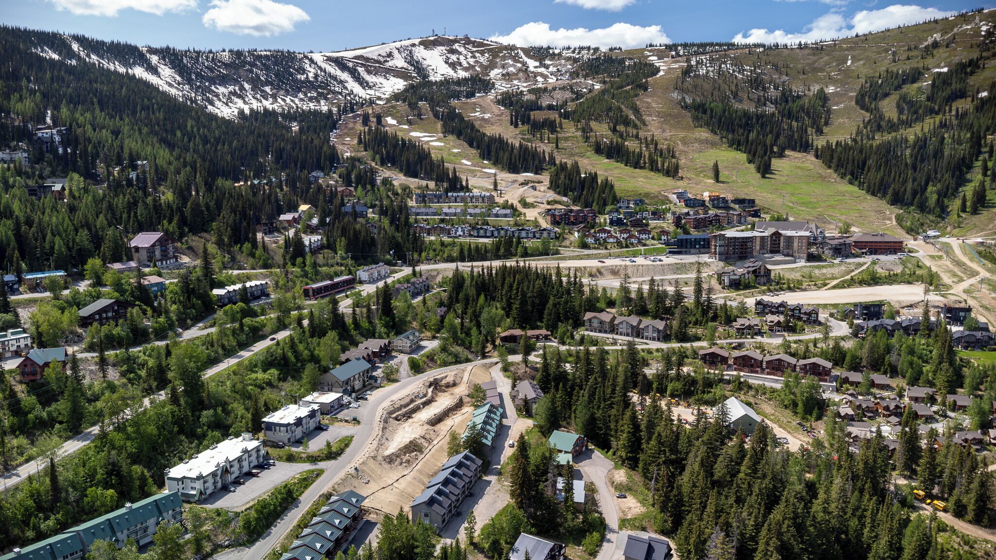 An aerial view of a mountain town with residential buildings, roads, and a ski slope.