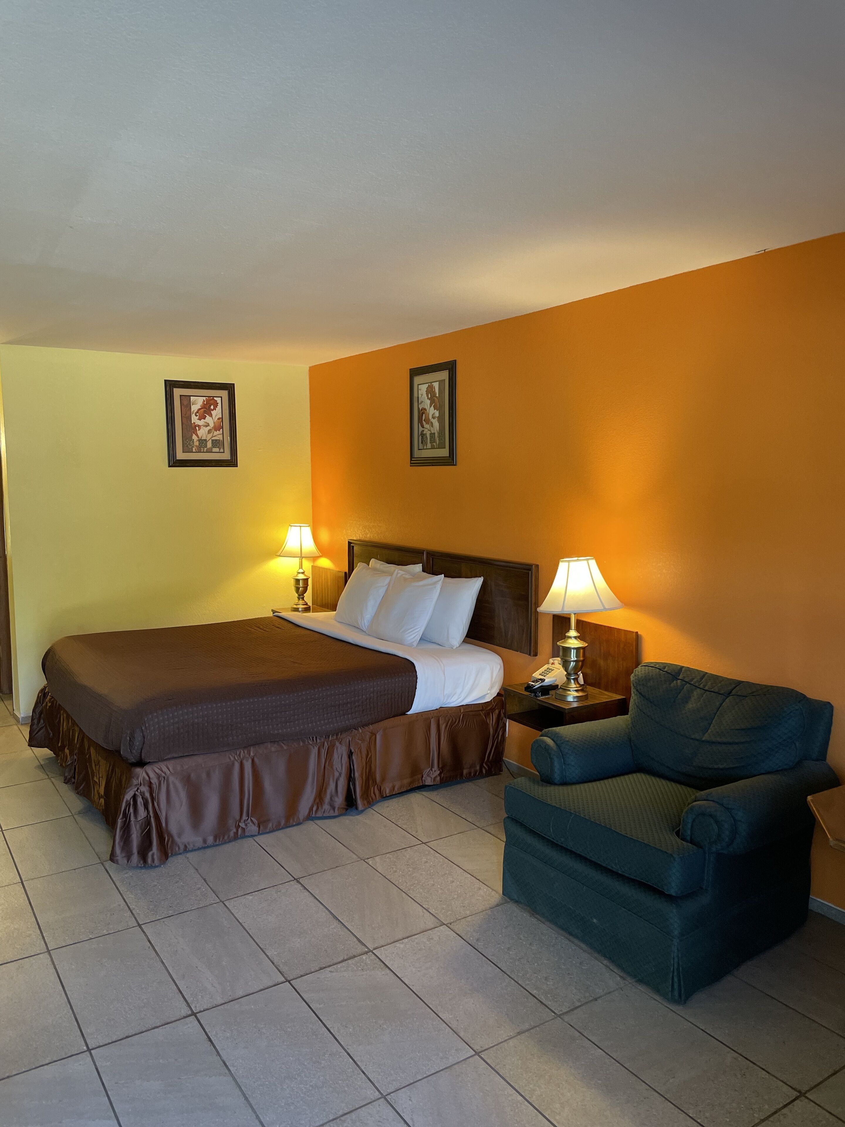 A hotel room with a bed, two bedside lamps, a chair, and two framed pictures on the walls.